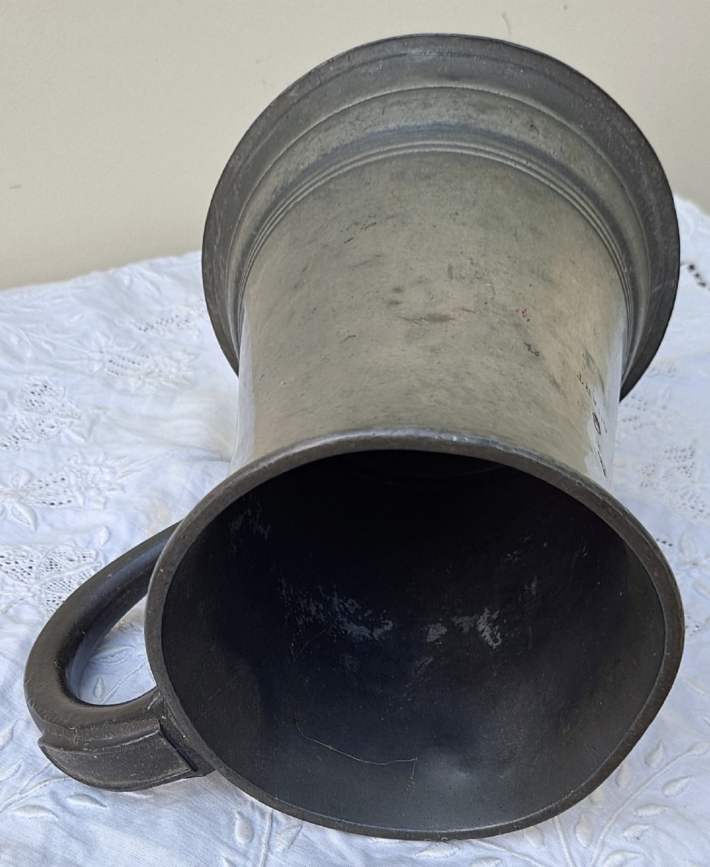 An antique Victorian pewter quart mug featuring a concave waist, flared base with moulded trim, and a dark curved loop handle. View V