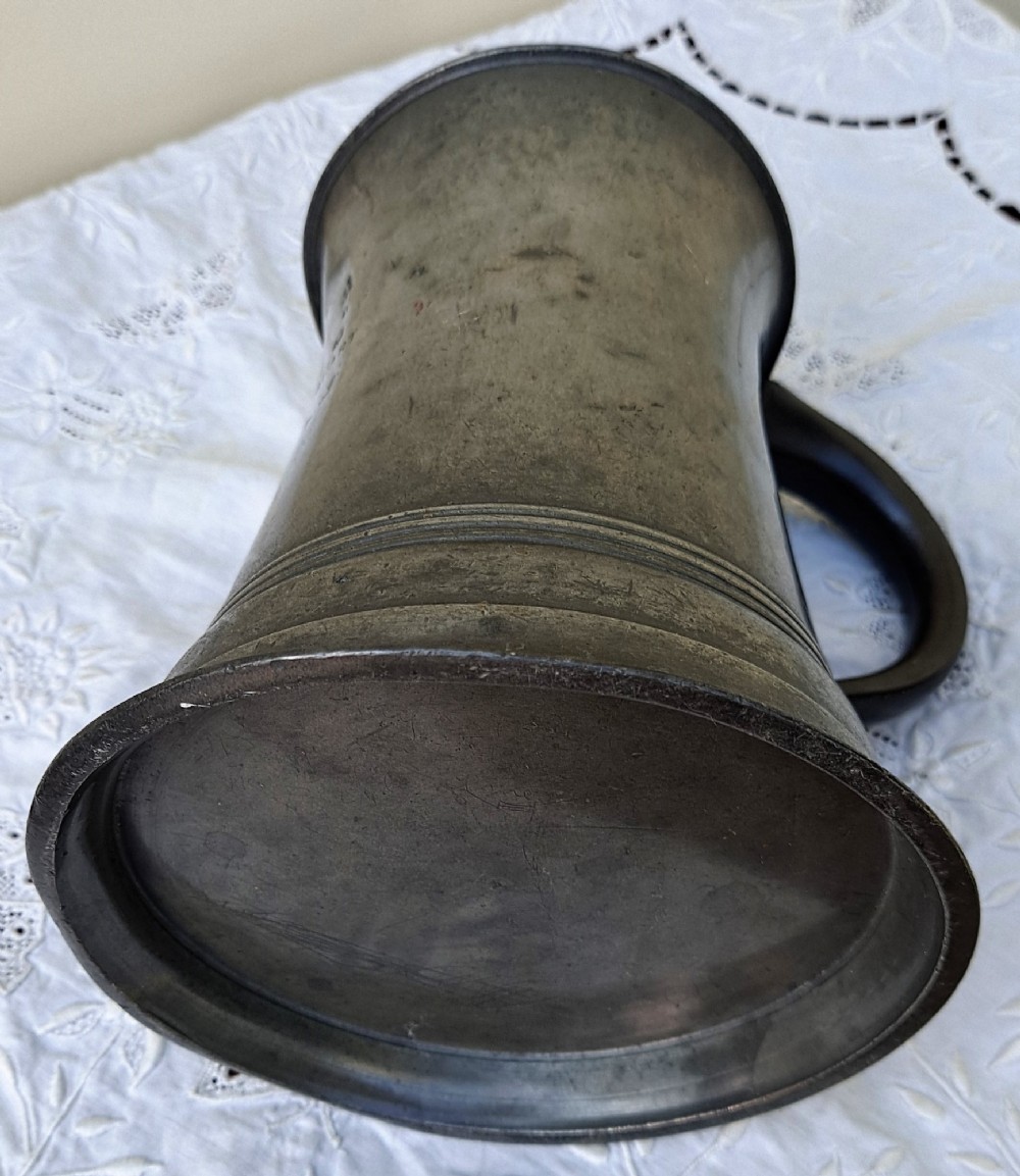 An antique Victorian pewter quart mug featuring a concave waist, flared base with moulded trim, and a dark curved loop handle. View VI