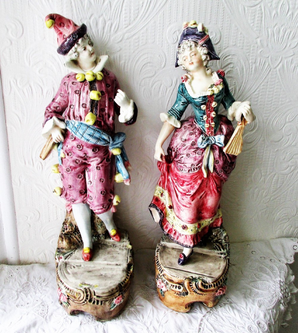 A pair of hand-painted French earthenware carnival figurines depicting a man and woman in colourful theatrical costumes standing on decorative plinth bases.