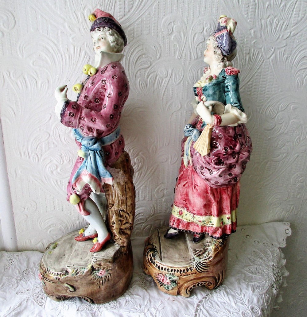 A pair of hand-painted French earthenware carnival figurines depicting a man and woman in colourful theatrical costumes standing on decorative plinth bases. View II