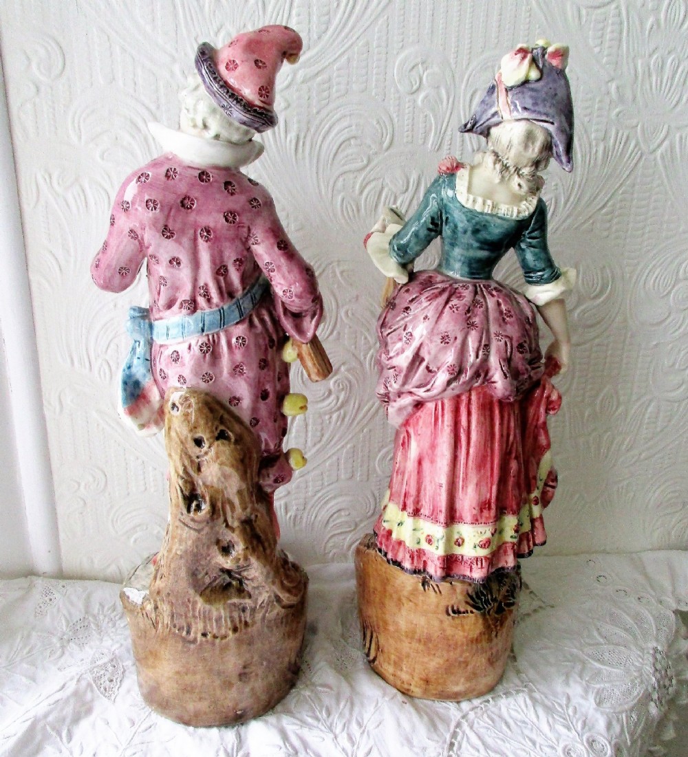 A pair of hand-painted French earthenware carnival figurines depicting a man and woman in colourful theatrical costumes standing on decorative plinth bases. View III