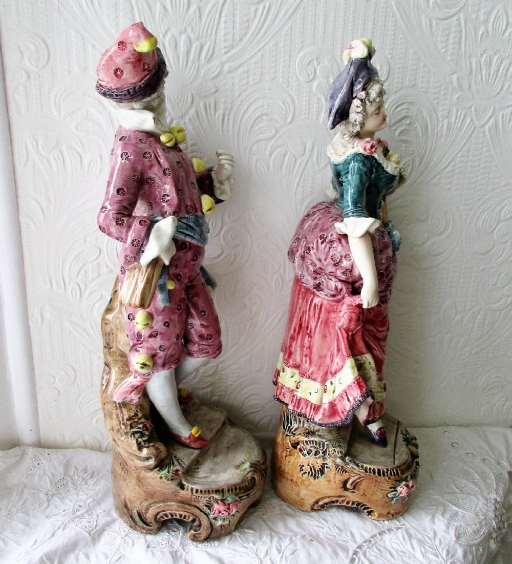 A pair of hand-painted French earthenware carnival figurines depicting a man and woman in colourful theatrical costumes standing on decorative plinth bases. View IV