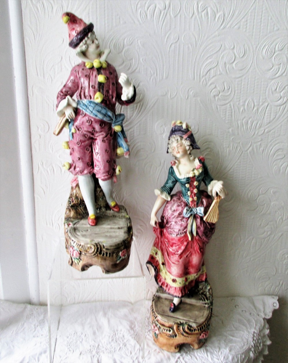 A pair of hand-painted French earthenware carnival figurines depicting a man and woman in colourful theatrical costumes standing on decorative plinth bases. View VI