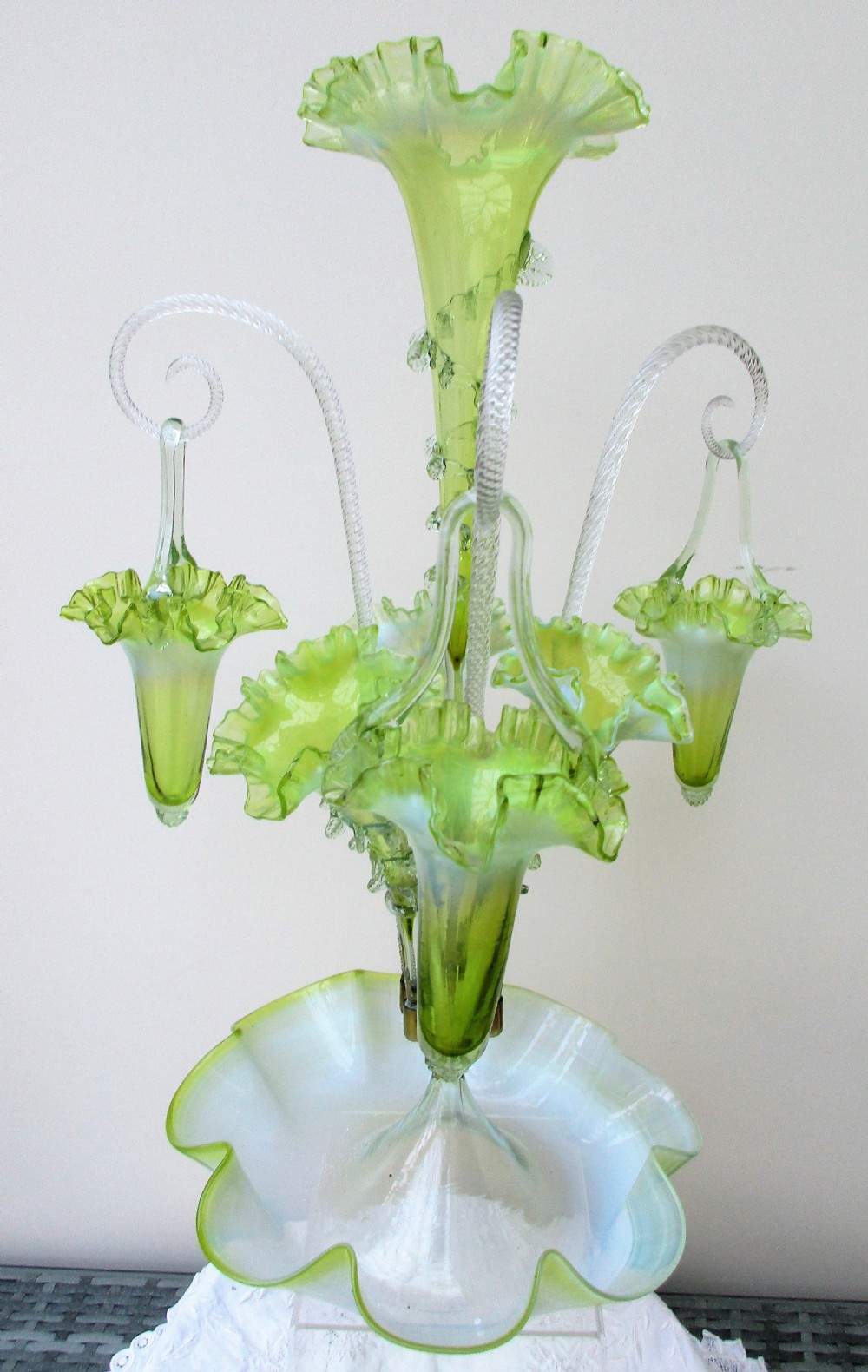 A Victorian vaseline glass epergne featuring a central ruffled trumpet vase, surrounding horns, hanging baskets, and a bowl base in yellow-green opalescent glass.