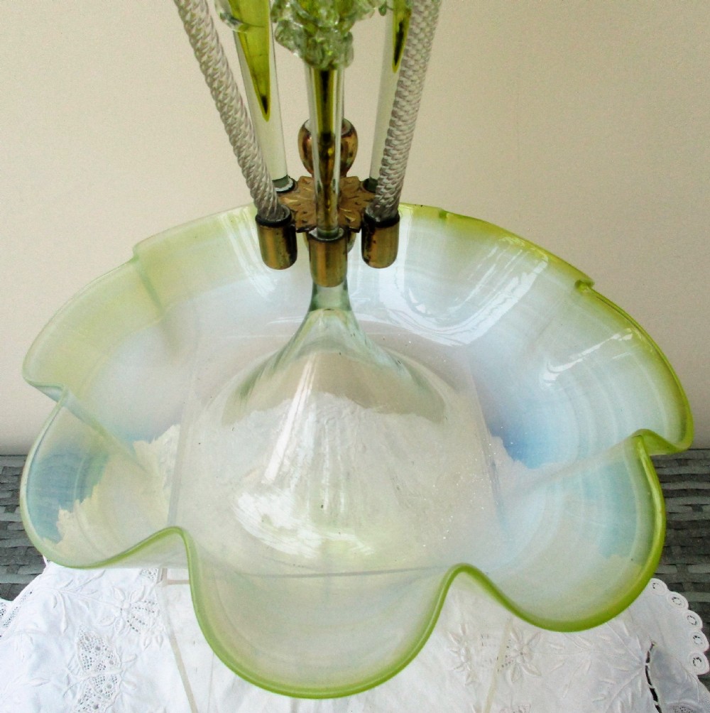 A Victorian vaseline glass epergne featuring a central ruffled trumpet vase, surrounding horns, hanging baskets, and a bowl base in yellow-green opalescent glass. View V