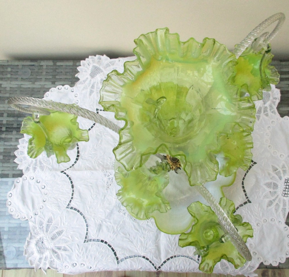 A Victorian vaseline glass epergne featuring a central ruffled trumpet vase, surrounding horns, hanging baskets, and a bowl base in yellow-green opalescent glass. View VI