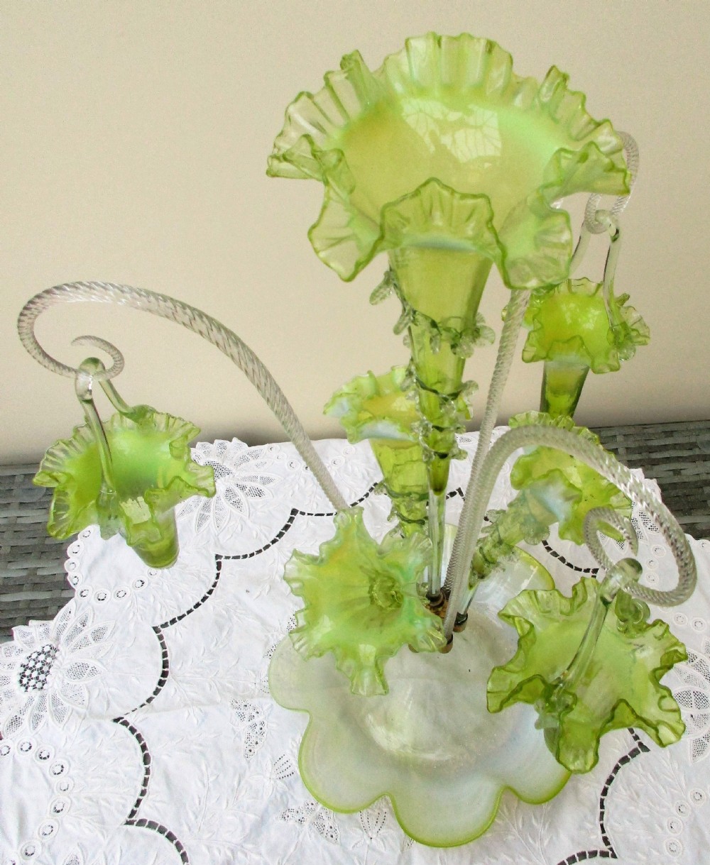 A Victorian vaseline glass epergne featuring a central ruffled trumpet vase, surrounding horns, hanging baskets, and a bowl base in yellow-green opalescent glass. View VII