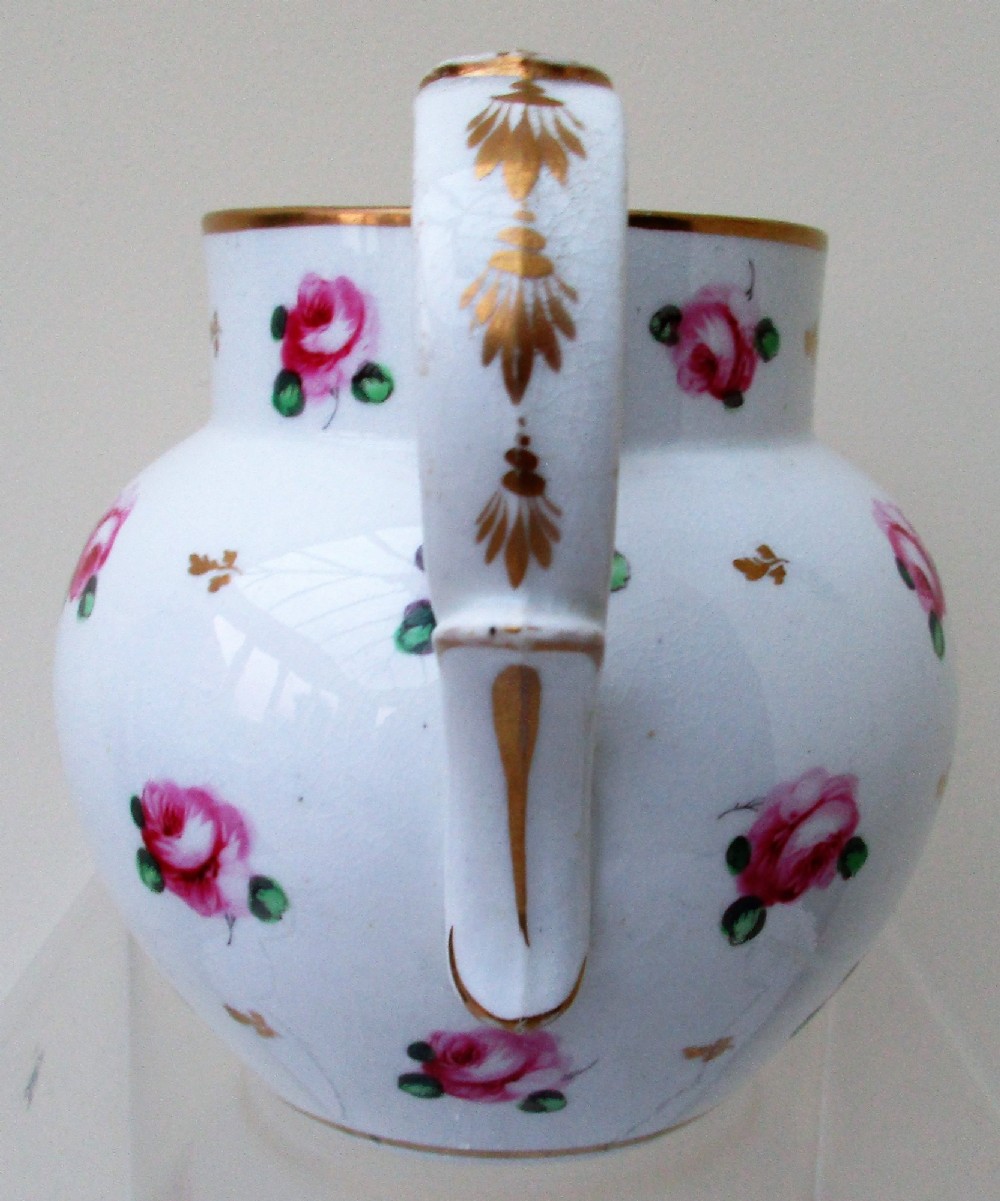 An antique white porcelain cream jug featuring hand-painted pink rose sprigs, gold leaf detailing, a pointed sparrow beak spout, and a curved handle. View II