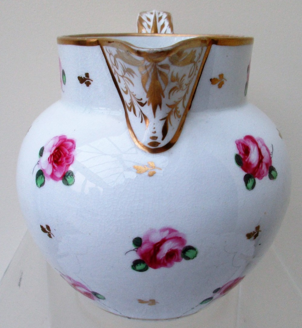 An antique white porcelain cream jug featuring hand-painted pink rose sprigs, gold leaf detailing, a pointed sparrow beak spout, and a curved handle. View IV