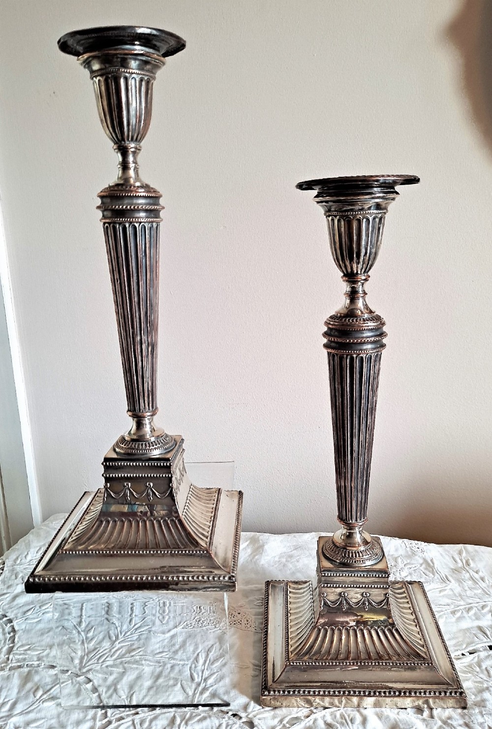 A pair of silver-plated Georgian candlesticks featuring fluted shafts, urn sconces, and square decorated bases showing copper wear. View II