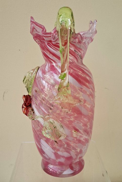 fig 1. A Victorian hand-blown glass vase featuring a pink swirled body, a ruffled rim, an applied red flower accent, and two green vaseline glass handles.