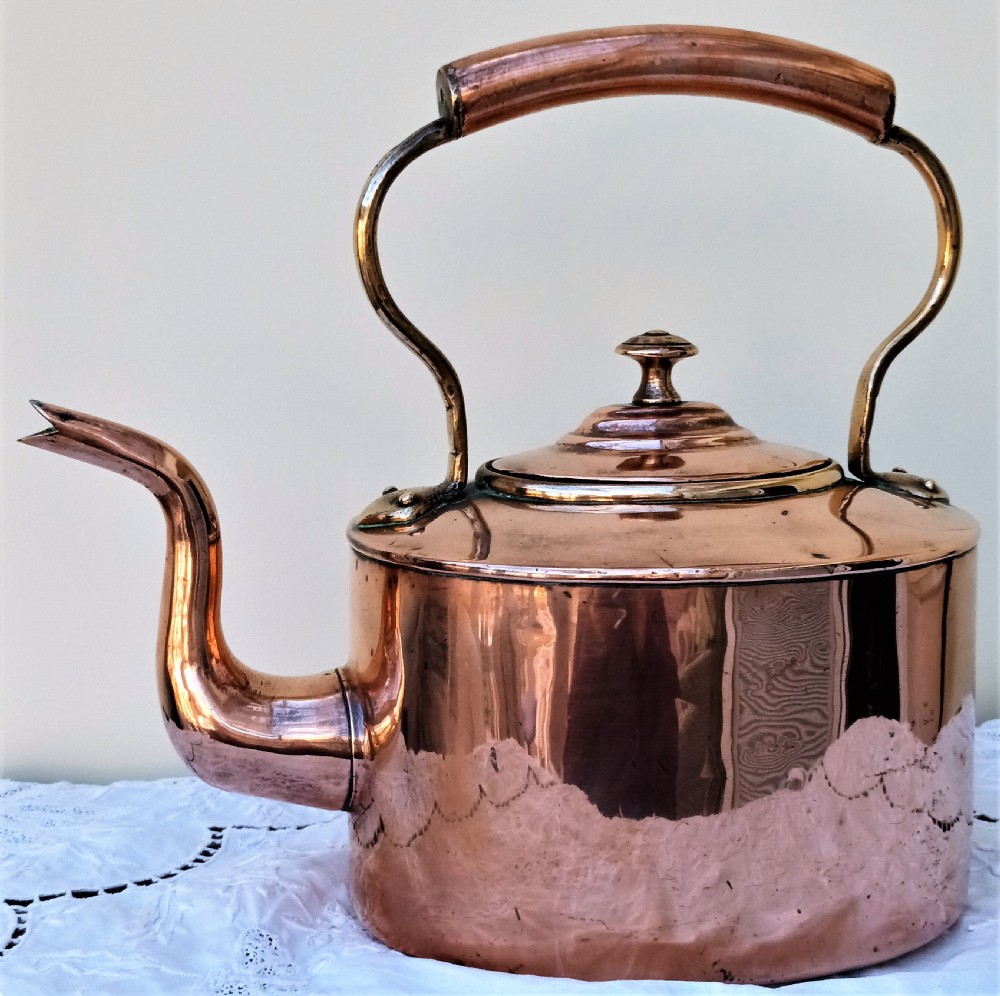 A polished Victorian copper kettle featuring a gooseneck spout, fitted circular lid with finial, and fixed overhead handle.