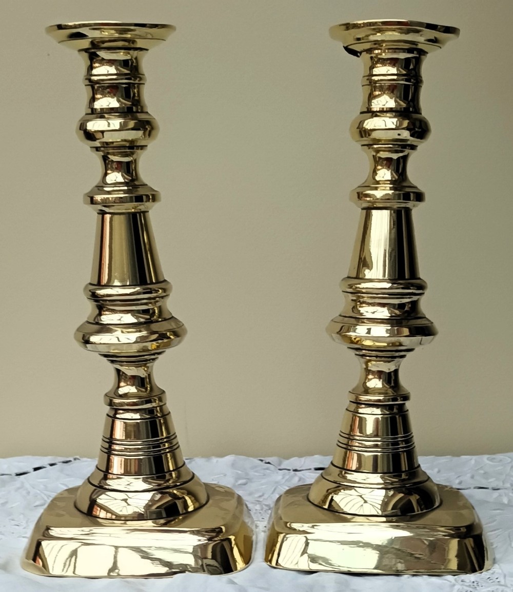 A pair of polished gold-toned brass Victorian candlesticks featuring turned baluster stems and square bases.