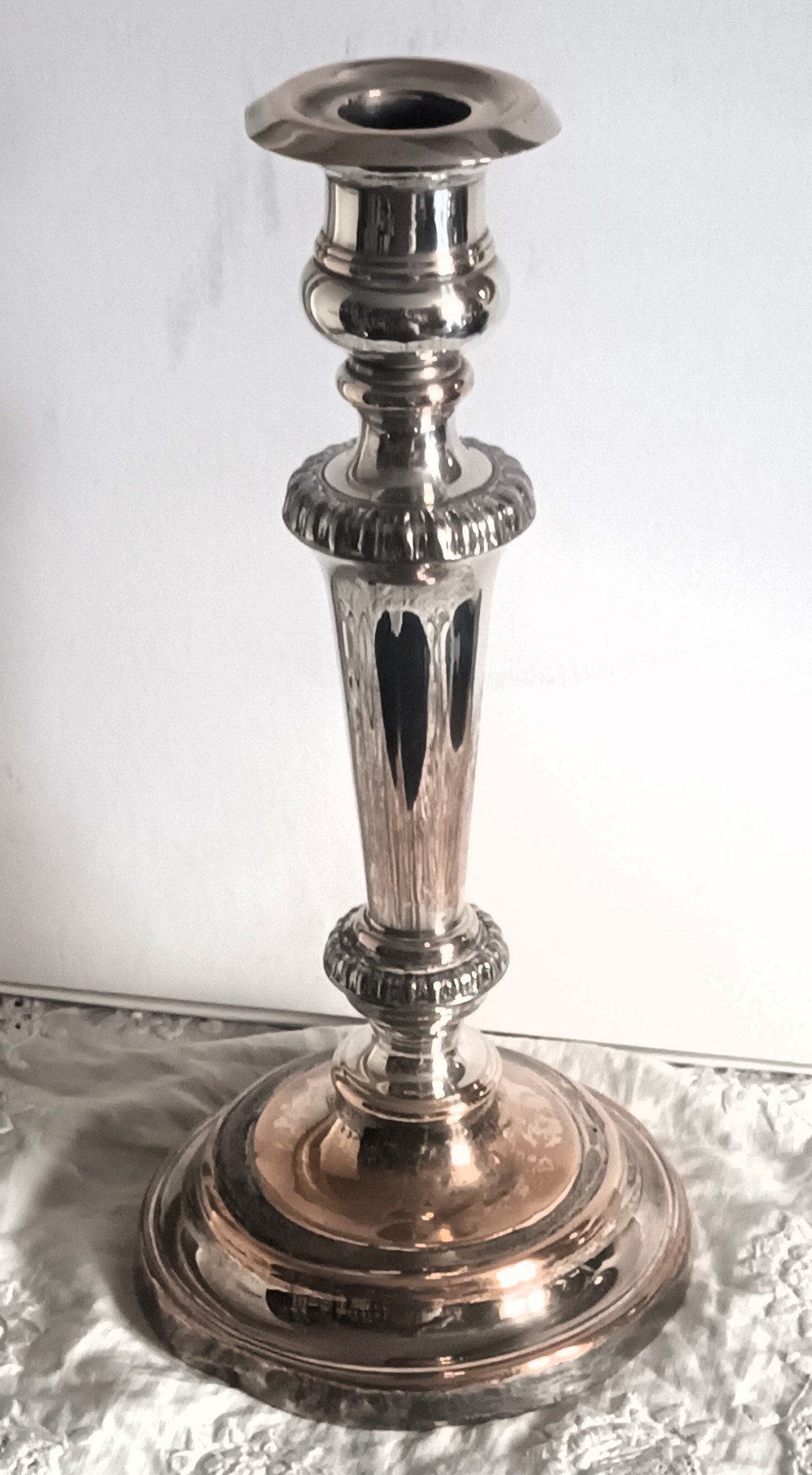 A single silver-plated candlestick featuring a turned circular base, gadrooned collar detailing, and subtle copper showing through worn areas.