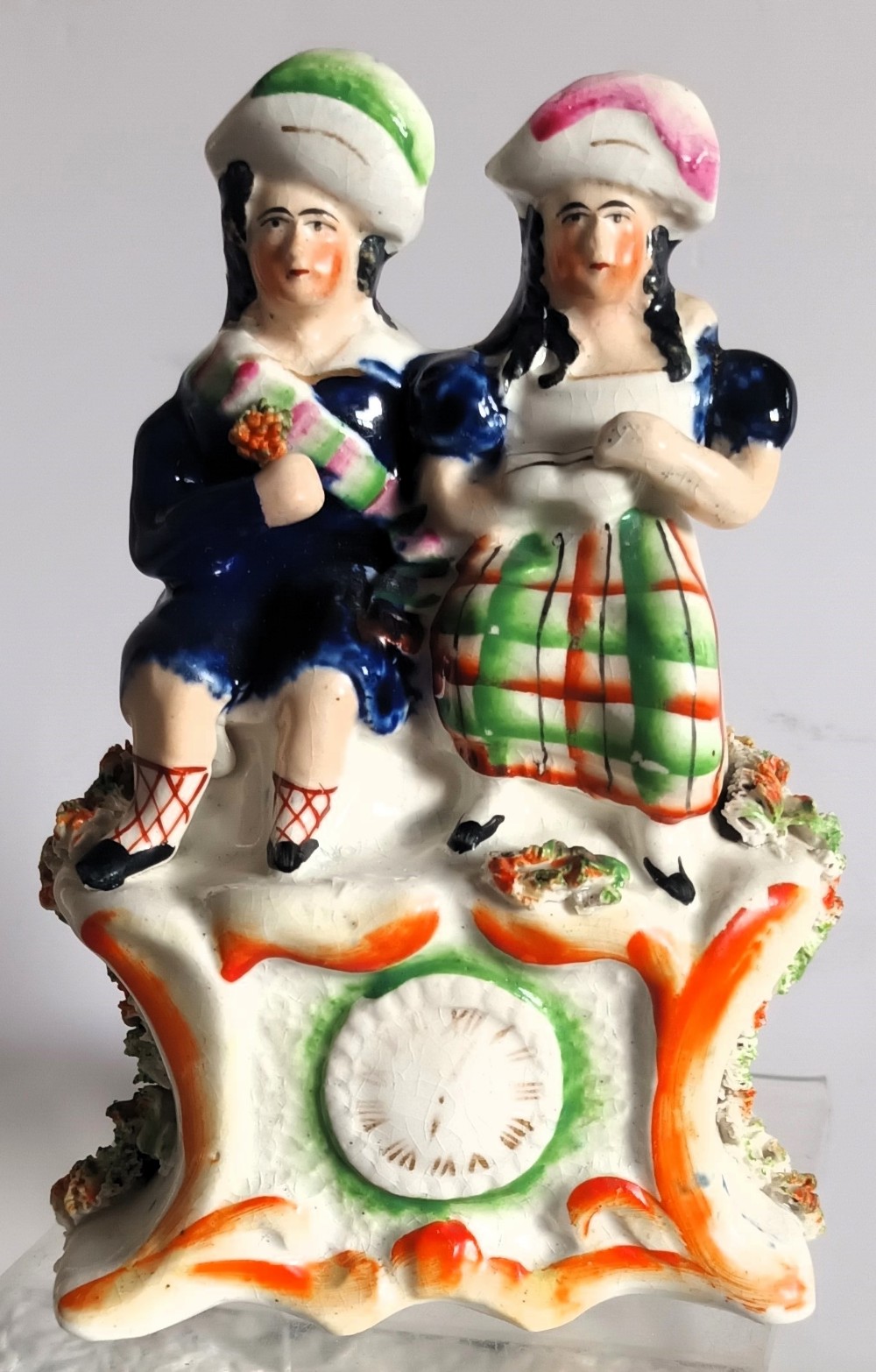 A Victorian Staffordshire pottery figurine depicting two seated figures in Scottish dress set above a painted clock face.