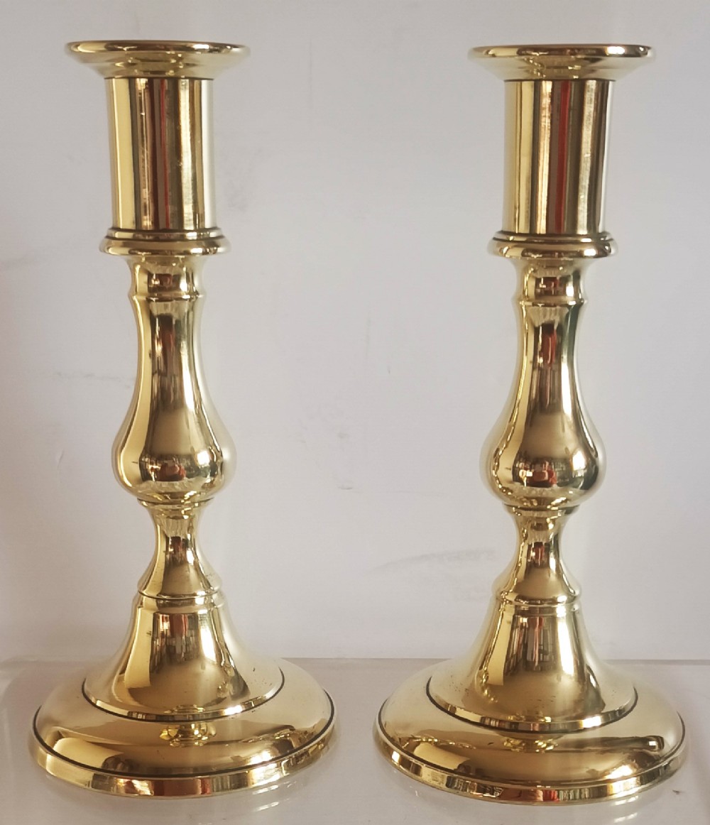 A pair of polished gold brass candlesticks featuring baluster turned stems and stepped circular bases.