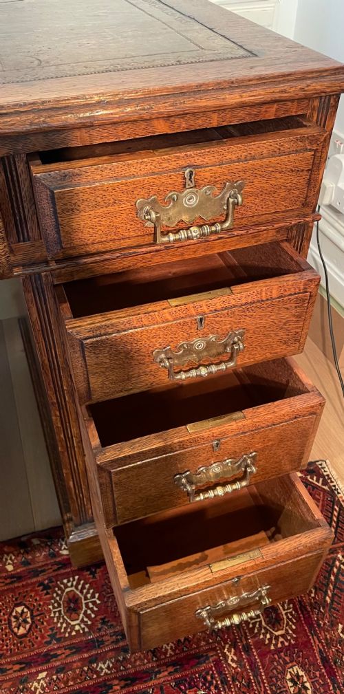 A Victorian oak pedestal desk featuring a gold-tooled leather writing top, nine drawers, and brass handles on a plinth base. View IX