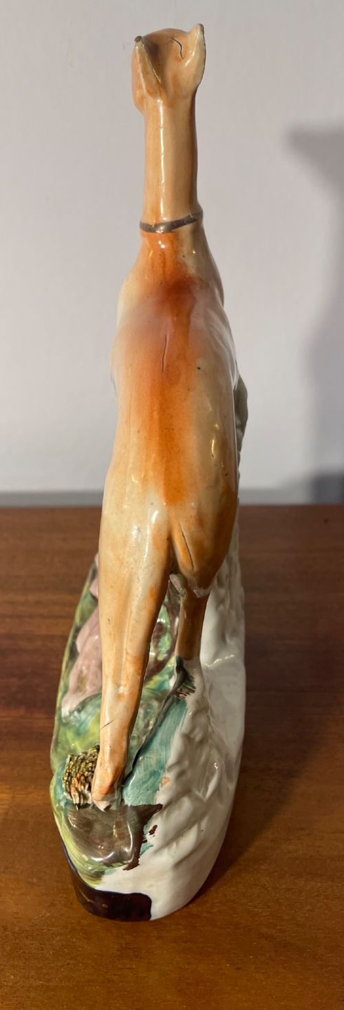 An antique Staffordshire earthenware figure depicting a standing tan hound with a crouching hare on a green and blue glazed base. View IX