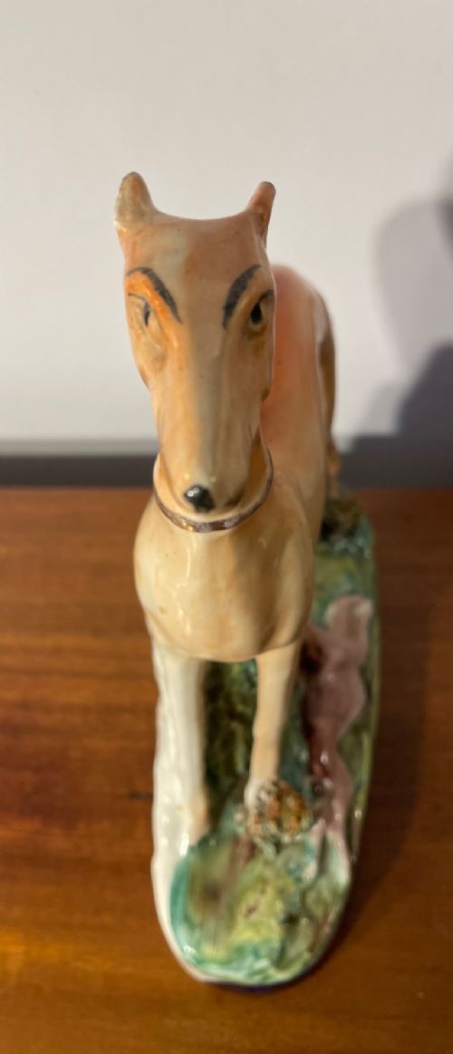 An antique Staffordshire earthenware figure depicting a standing tan hound with a crouching hare on a green and blue glazed base. View XI