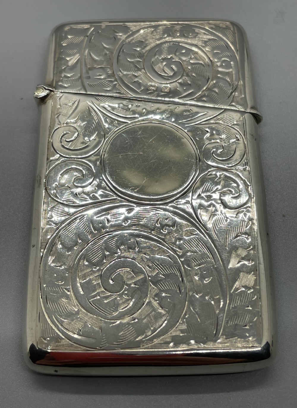 An engraved sterling silver card case featuring scrollwork patterns and a central circular cartouche.