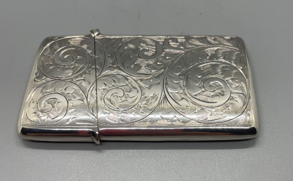 An engraved sterling silver card case featuring scrollwork patterns and a central circular cartouche. View IV