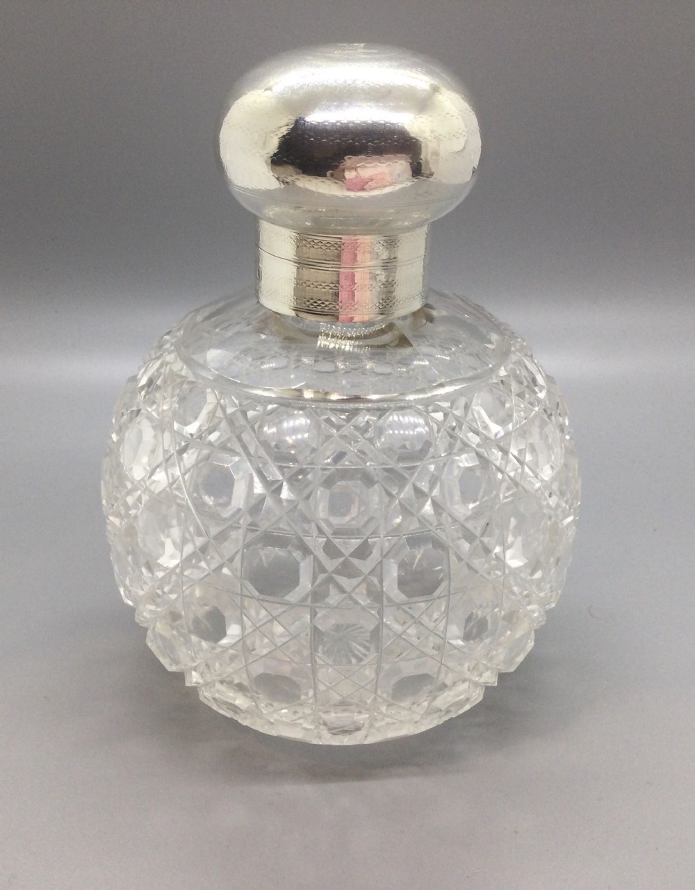 A round cut glass scent bottle with a polished globe-shaped sterling silver top.