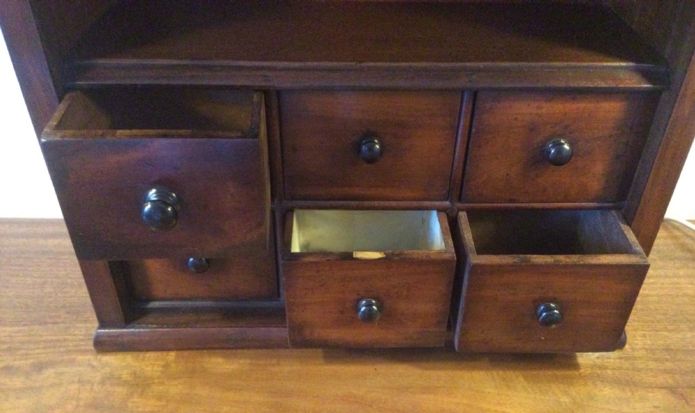 A mid-19th-century mahogany wall-hanging shelf unit featuring an open upper section above six small drawers with turned wooden knobs. View VI