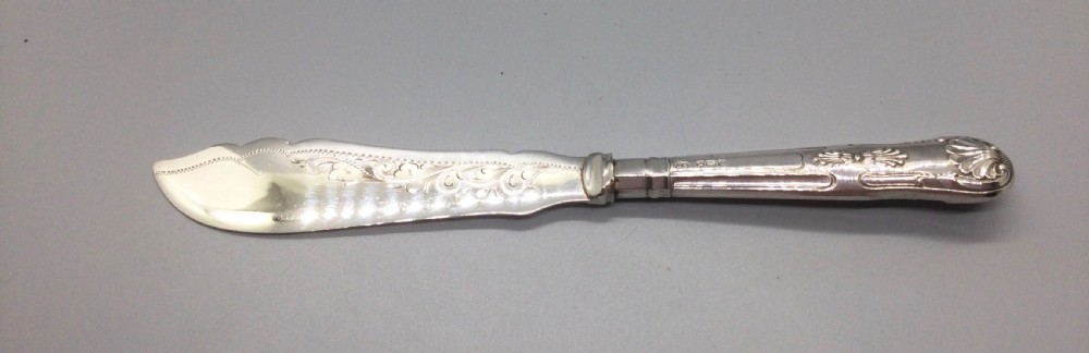 A three-piece Edwardian sterling silver serving set comprising a butter knife, pickle fork, and preserve spoon housed inside an open red velvet-lined presentation case. View III
