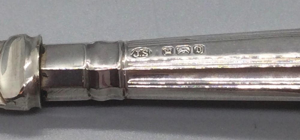 A three-piece Edwardian sterling silver serving set comprising a butter knife, pickle fork, and preserve spoon housed inside an open red velvet-lined presentation case. View IV