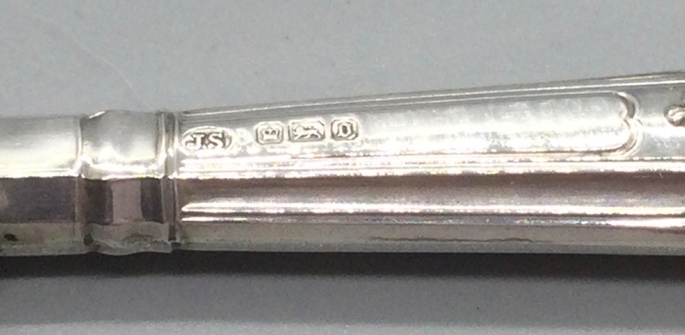 A three-piece Edwardian sterling silver serving set comprising a butter knife, pickle fork, and preserve spoon housed inside an open red velvet-lined presentation case. View VI