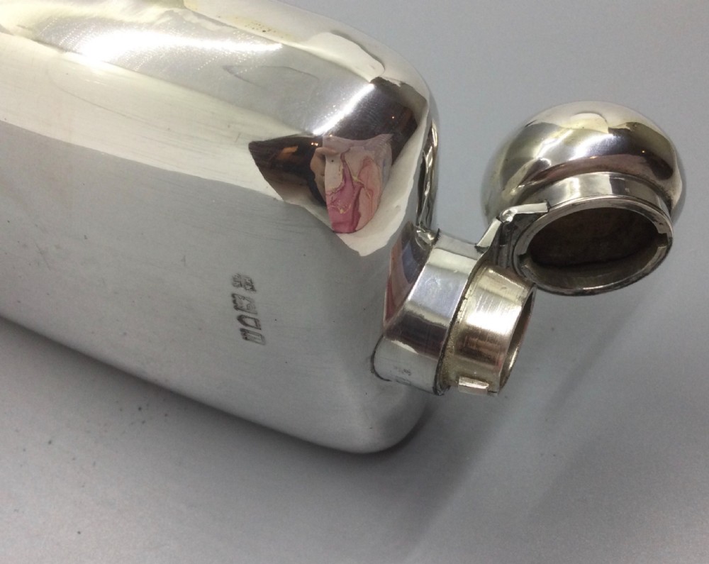 A curved rectangular sterling silver Edwardian spirit flask with a rounded domed cap and visible British hallmarks stamped near the shoulder. View VI