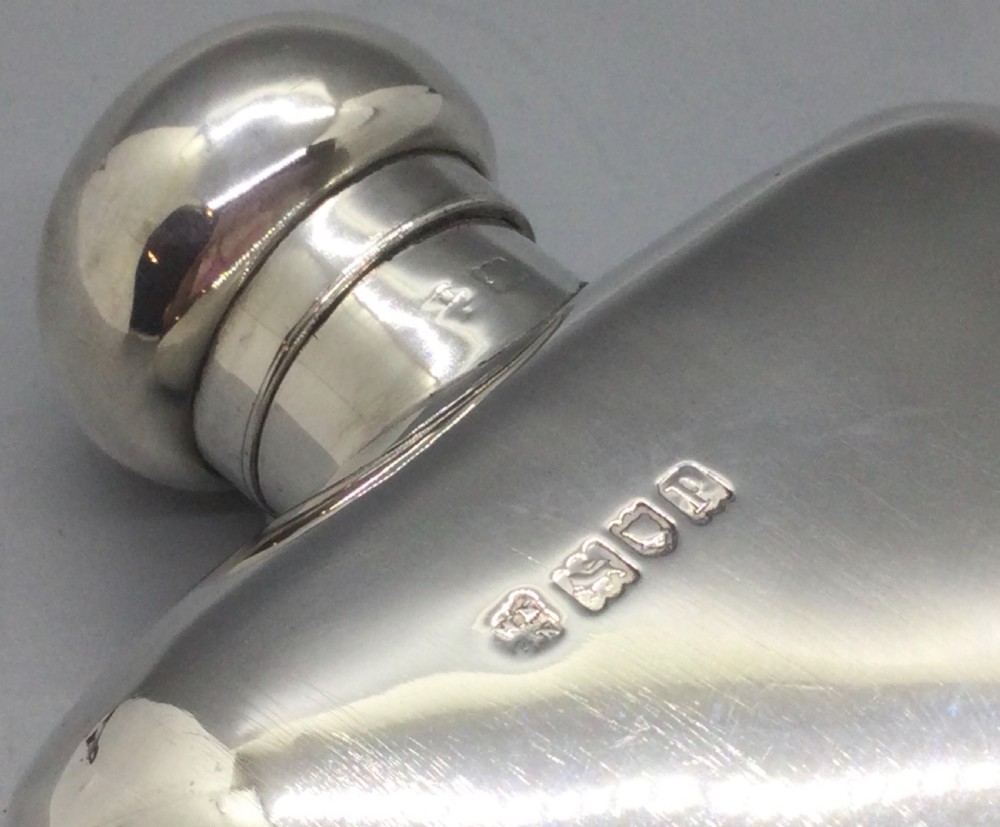 A curved rectangular sterling silver Edwardian spirit flask with a rounded domed cap and visible British hallmarks stamped near the shoulder. View VII