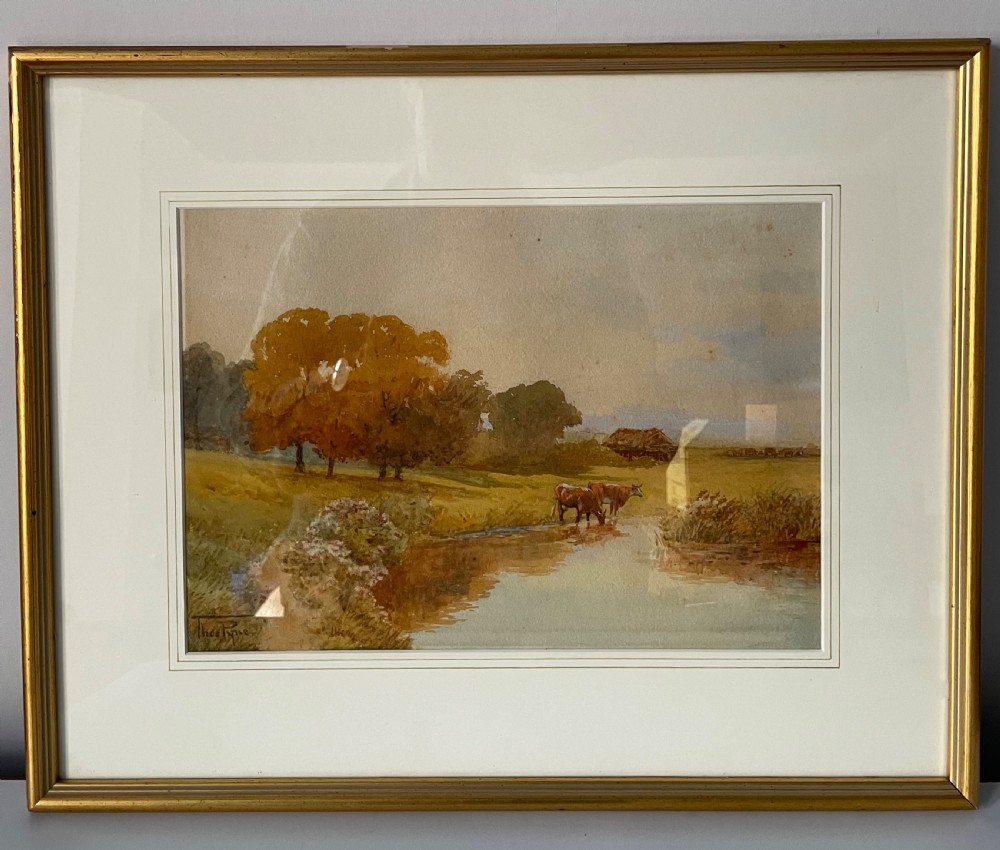 A framed watercolour painting showing cattle watering in a river bordered by green trees and fields, encased in a slim gold frame.