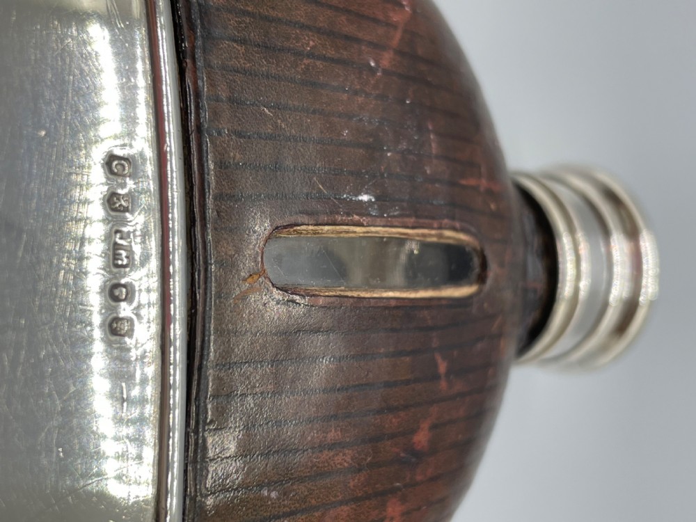 A Victorian spirit flask featuring a glass body encased in dark brown leather with a central sight window and a polished silver lower cup and cap. View III