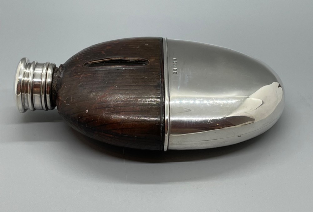 A Victorian spirit flask featuring a glass body encased in dark brown leather with a central sight window and a polished silver lower cup and cap. View V