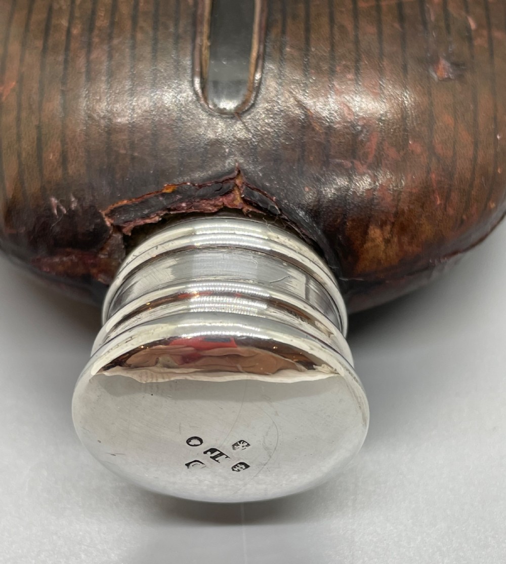 A Victorian spirit flask featuring a glass body encased in dark brown leather with a central sight window and a polished silver lower cup and cap. View VI