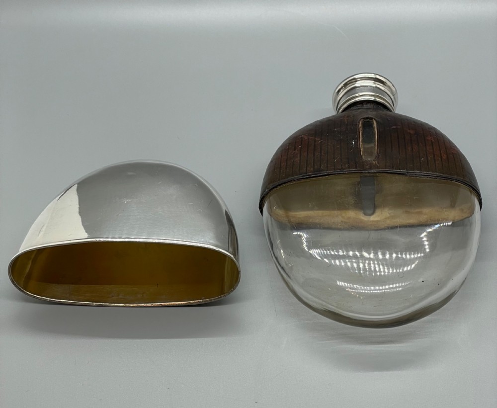 A Victorian spirit flask featuring a glass body encased in dark brown leather with a central sight window and a polished silver lower cup and cap. View VII