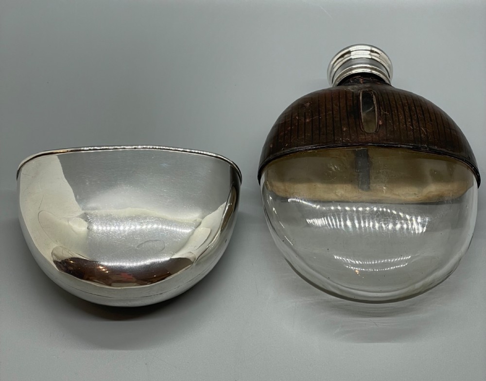 A Victorian spirit flask featuring a glass body encased in dark brown leather with a central sight window and a polished silver lower cup and cap. View VIII