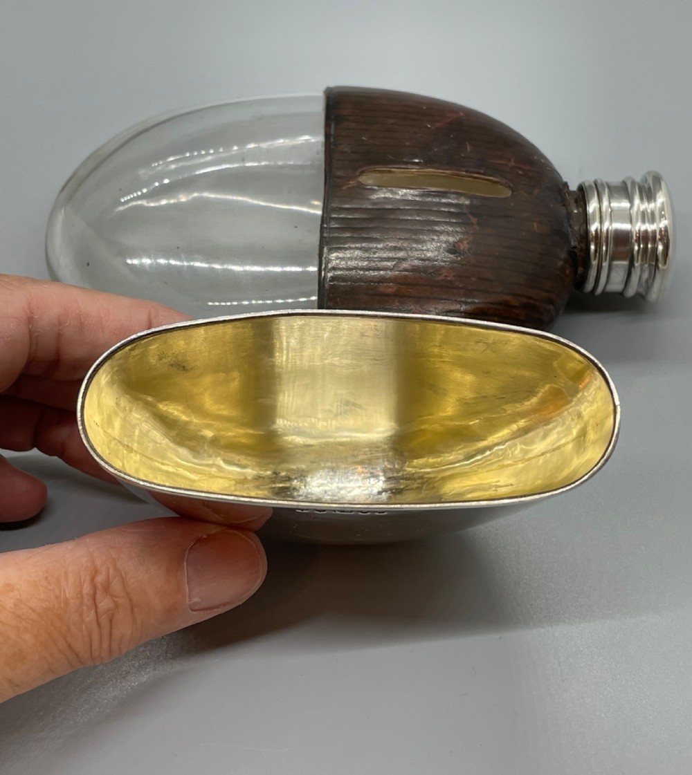 A Victorian spirit flask featuring a glass body encased in dark brown leather with a central sight window and a polished silver lower cup and cap. View IX