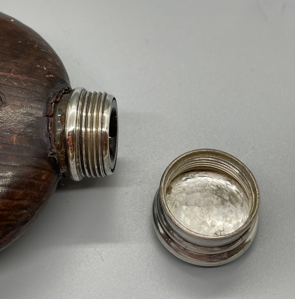 A Victorian spirit flask featuring a glass body encased in dark brown leather with a central sight window and a polished silver lower cup and cap. View XI