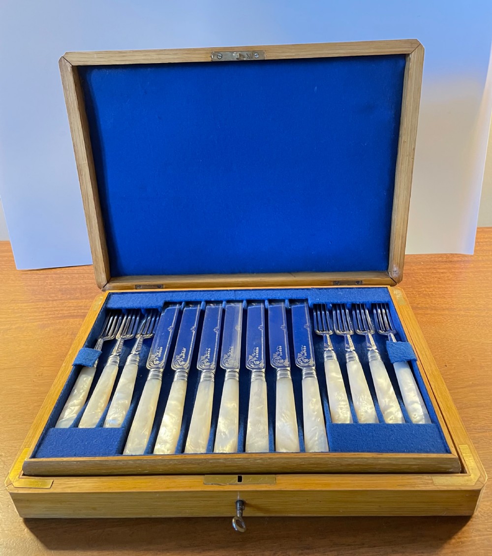 A Victorian silver-plated fruit cutlery set with mother-of-pearl handles displayed inside an open, blue velvet-lined wooden case.