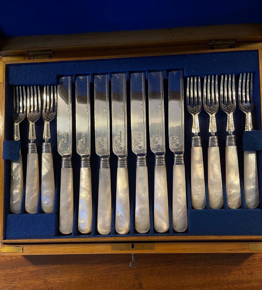 A Victorian silver-plated fruit cutlery set with mother-of-pearl handles displayed inside an open, blue velvet-lined wooden case. View III