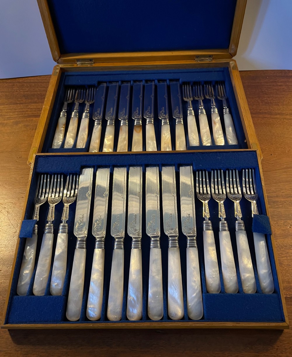 A Victorian silver-plated fruit cutlery set with mother-of-pearl handles displayed inside an open, blue velvet-lined wooden case. View IV
