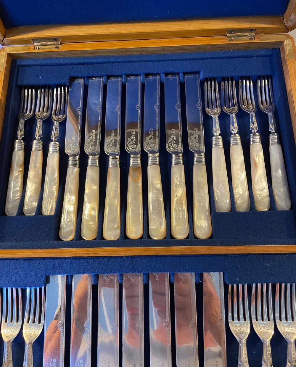 A Victorian silver-plated fruit cutlery set with mother-of-pearl handles displayed inside an open, blue velvet-lined wooden case. View V
