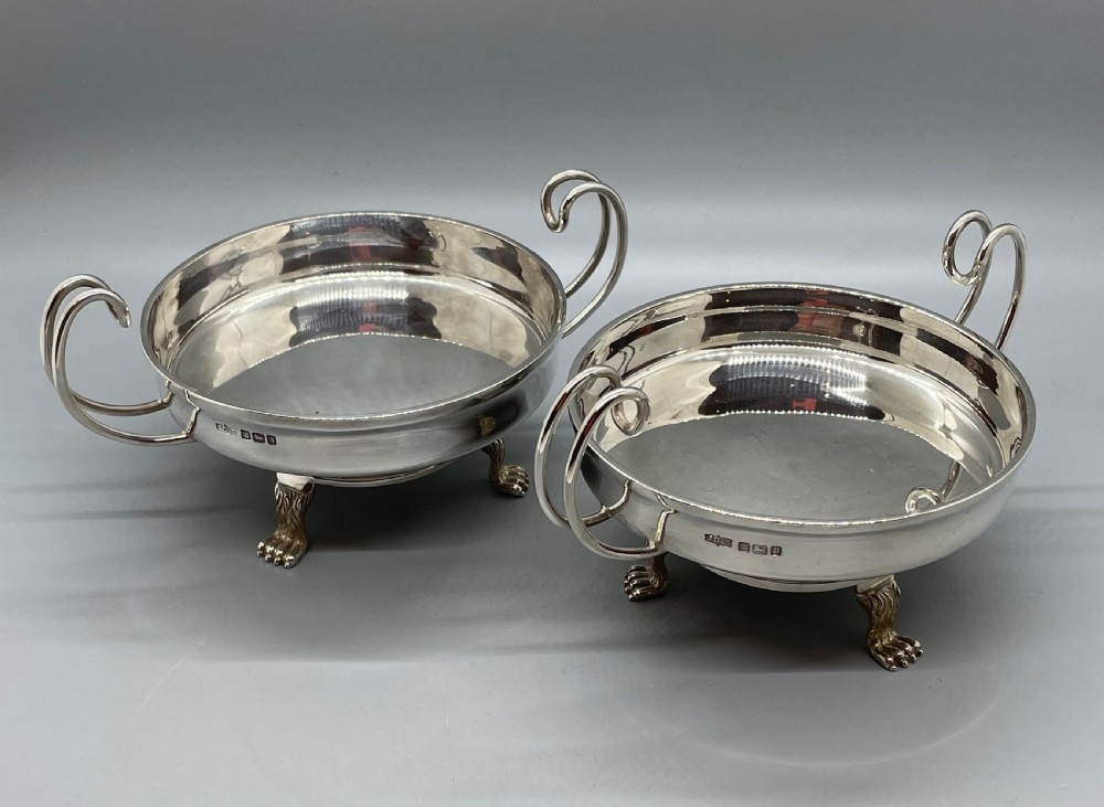 A pair of round Art Deco sterling silver bonbon dishes featuring twin scroll handles, lion paw feet, and visible Sheffield hallmarks. View II