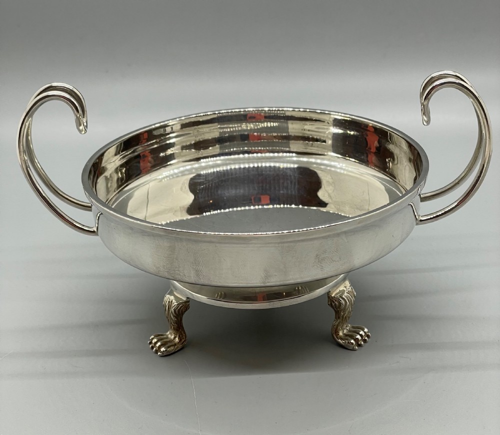 A pair of round Art Deco sterling silver bonbon dishes featuring twin scroll handles, lion paw feet, and visible Sheffield hallmarks. View IX