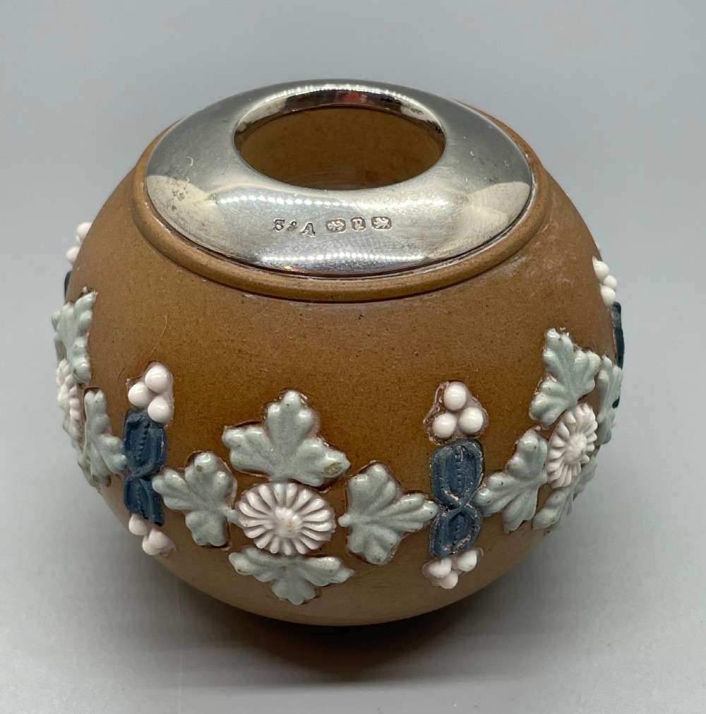 A spherical brown stoneware Victorian match striker featuring raised floral relief decoration and a polished sterling silver collar rim. View II