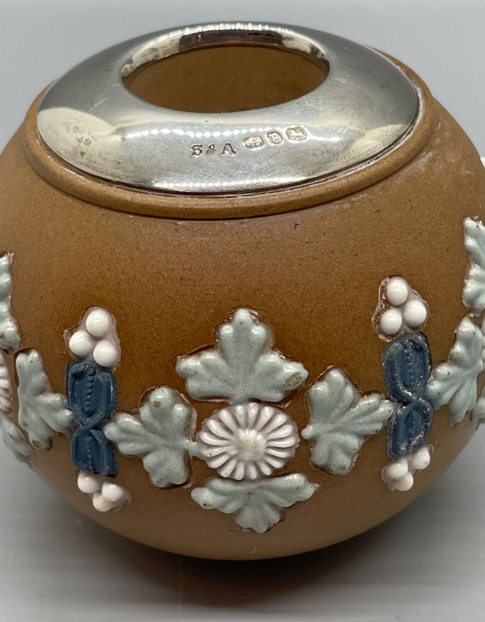 A spherical brown stoneware Victorian match striker featuring raised floral relief decoration and a polished sterling silver collar rim. View VI