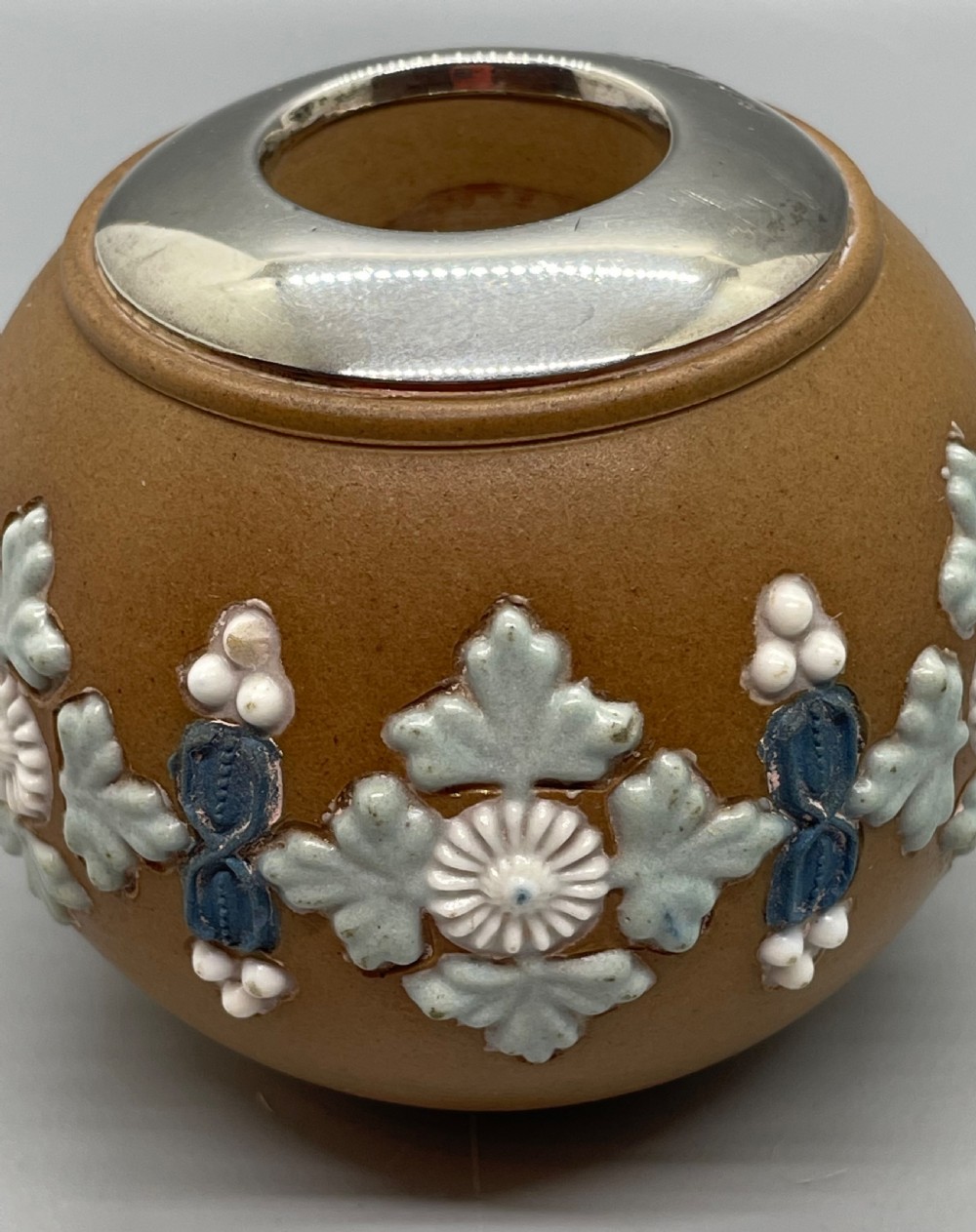 A spherical brown stoneware Victorian match striker featuring raised floral relief decoration and a polished sterling silver collar rim. View VII