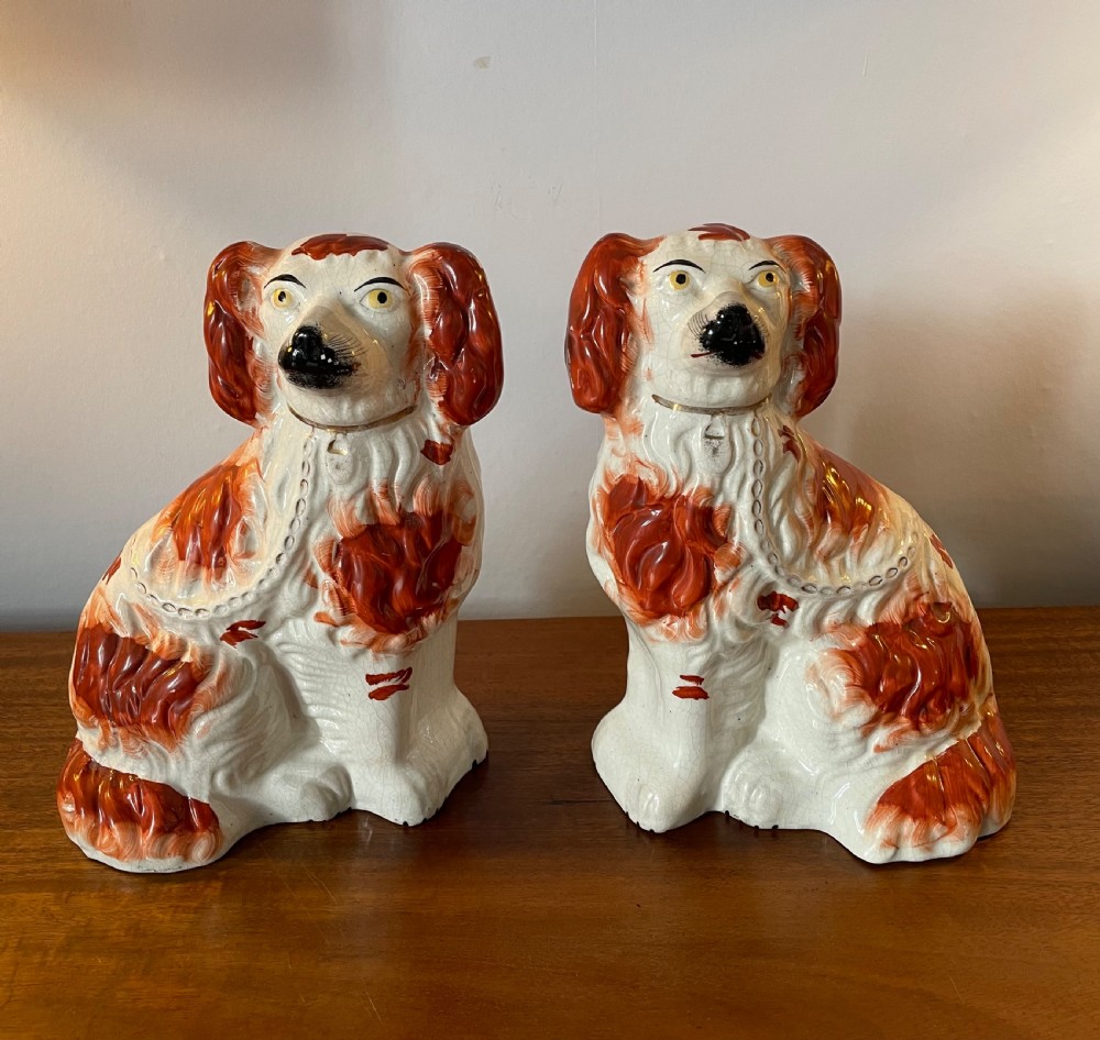 A pair of seated Victorian Staffordshire earthenware spaniel figurines featuring white glazed bodies with rust-red painted patches, black snouts, and gilded collars.
